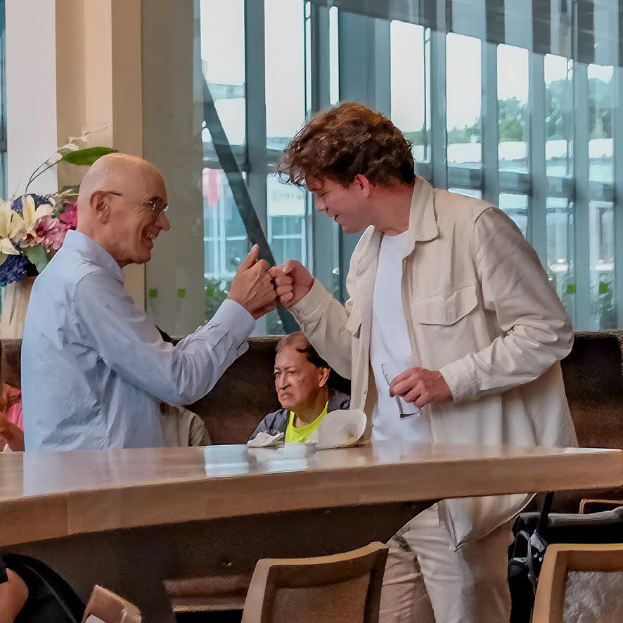 A younger and an older man greeting each other enthusiastically with a fist bump at a Wel zo Roze gathering