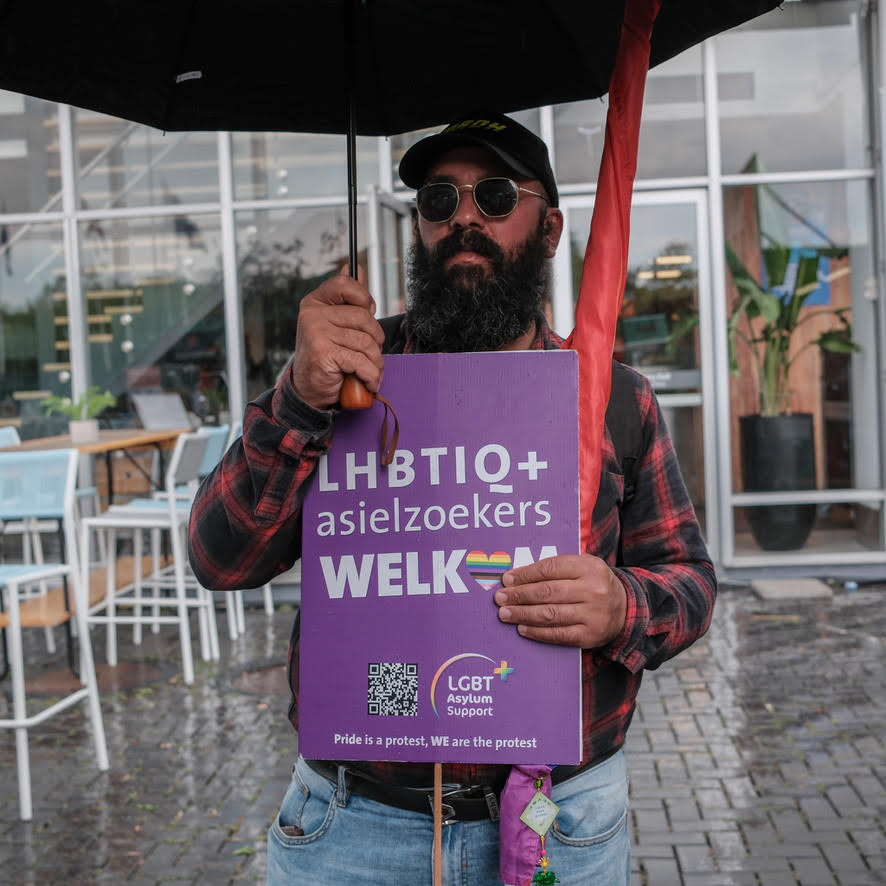 Man met een bord waarop staat 'LHBTIQ+ asielzoekers welkom'