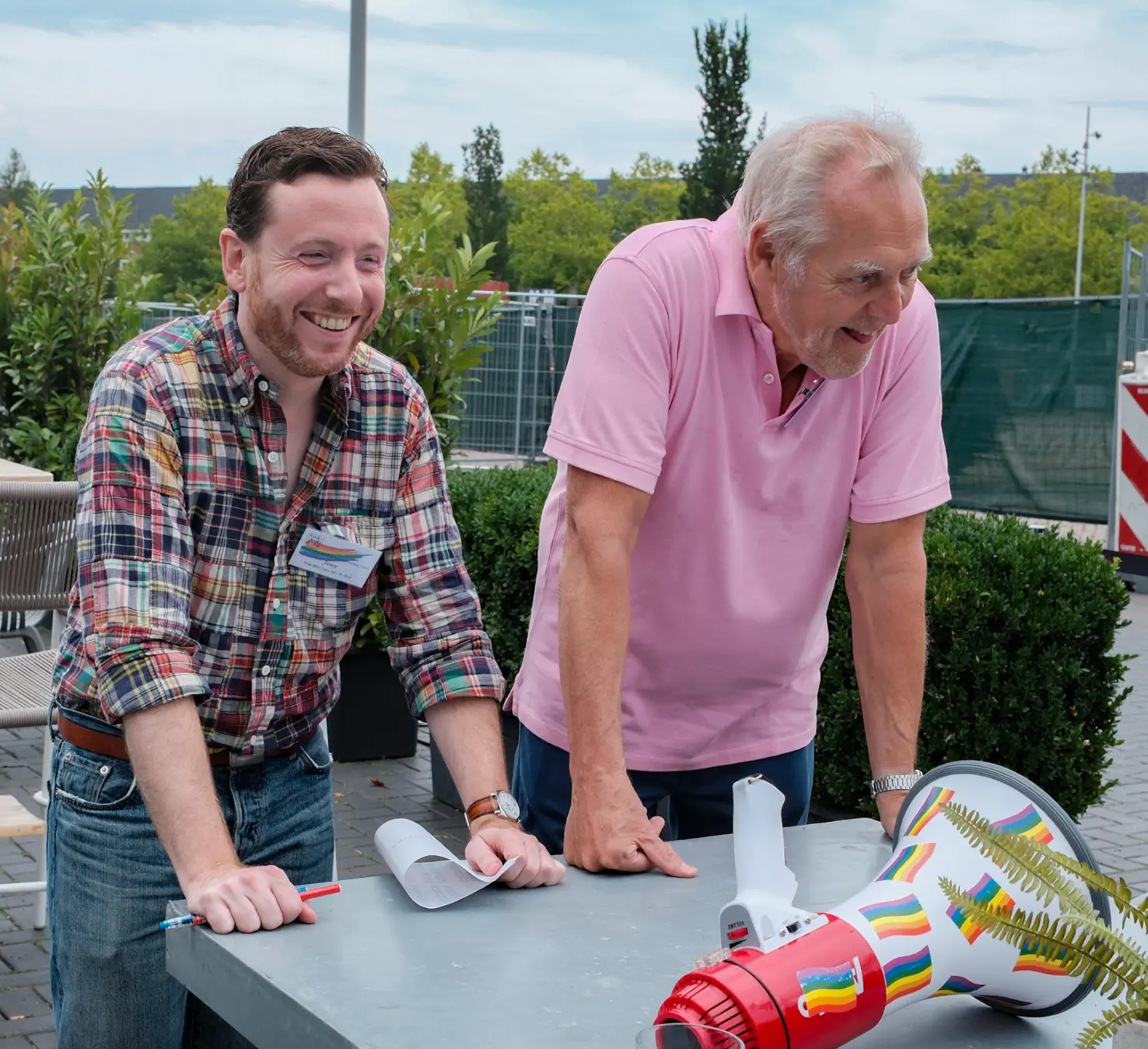 Joey Duis and a guest laughing together next to a rainbow megaphone at a Wel zo Roze gathering