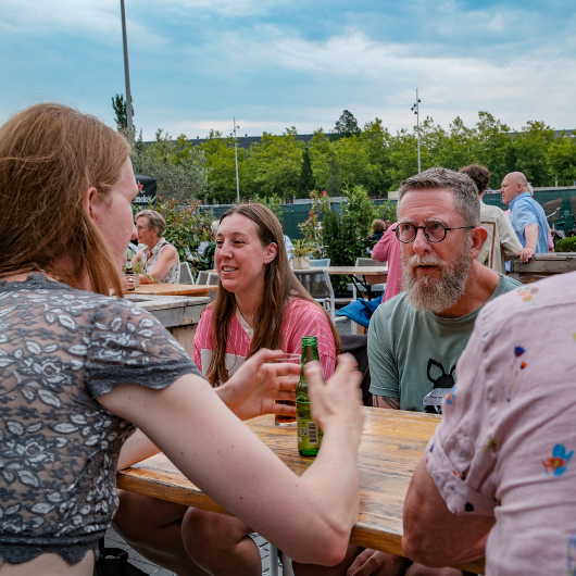 Mensen in gesprek aan een tuintafel tijdens een ontmoetingsbijeenkomst
