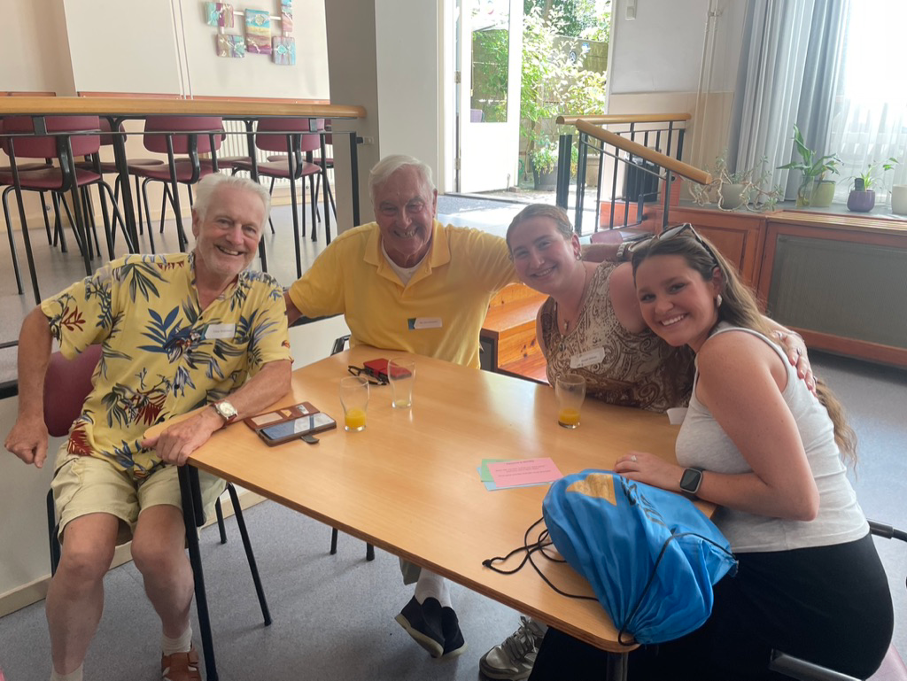 Four Wel zo Roze guests smiling together at a table during a community gathering