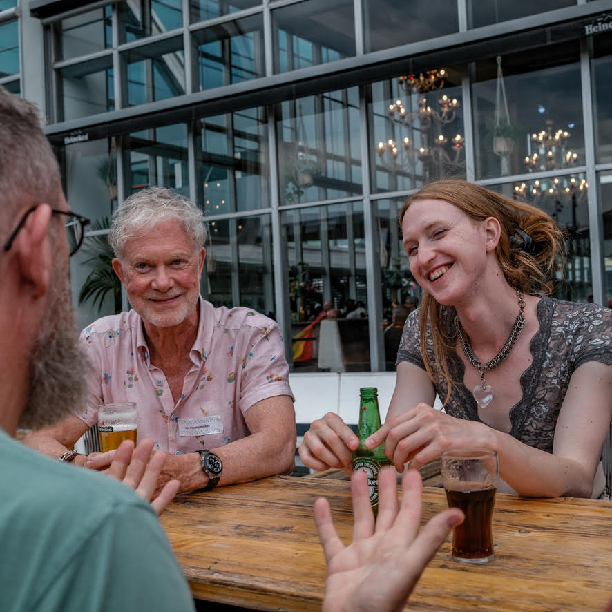Drie mensen in gesprek aan een houten tafel op een terras